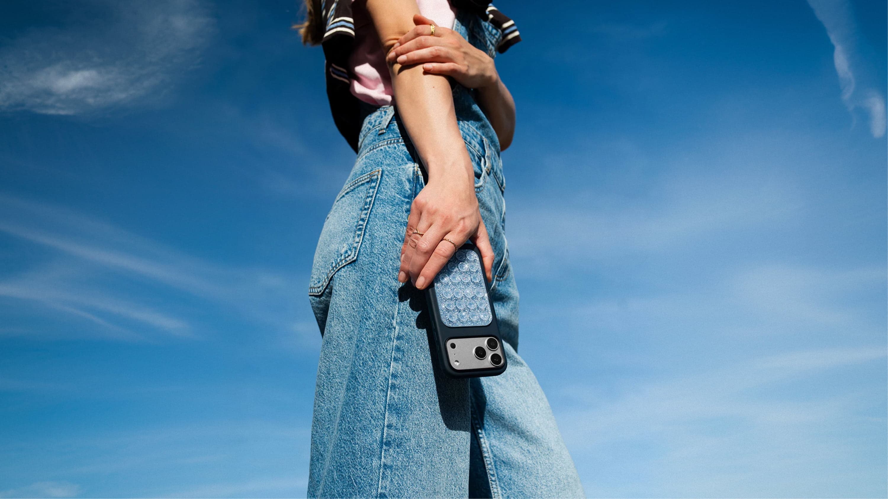 A person wearing blue denim jeans is holding a smartphone with an Octobuddy sticky attachment on the case.