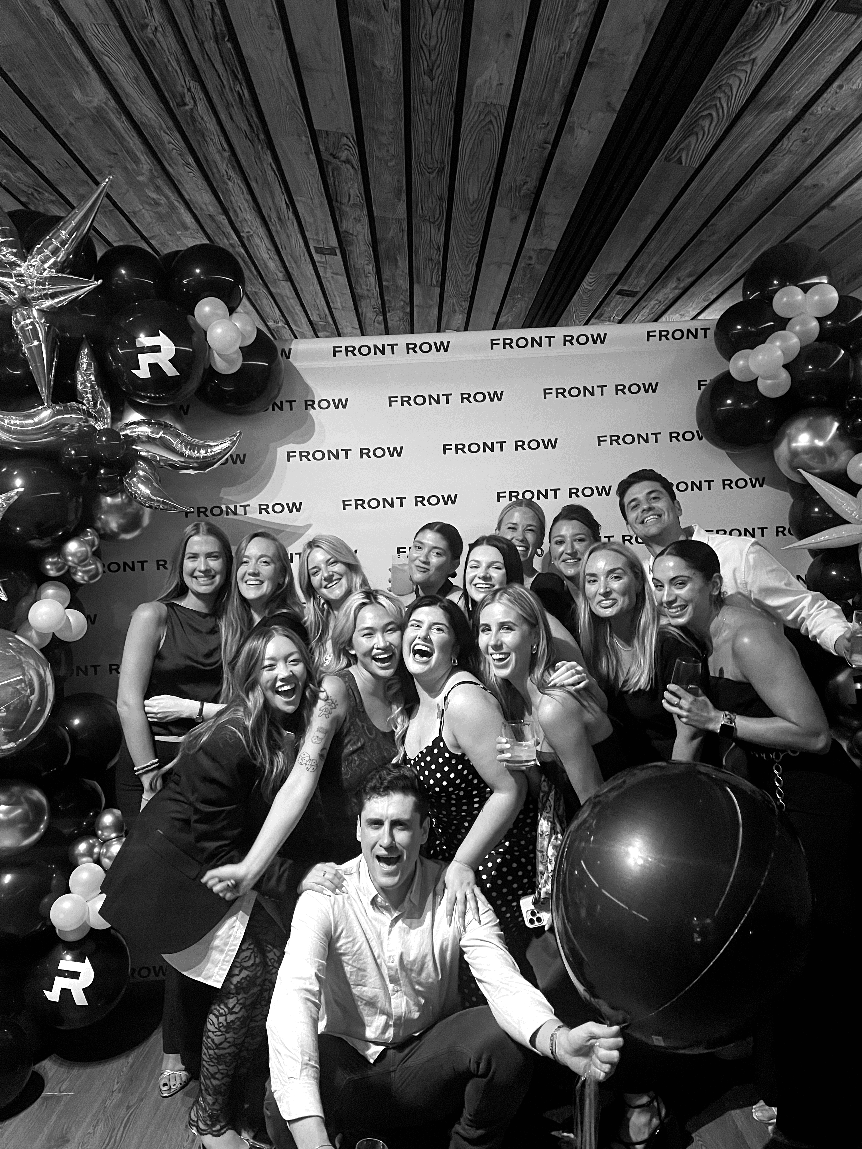 Front Row team members celebrate and pose for a photo in front of a Front Row press wall